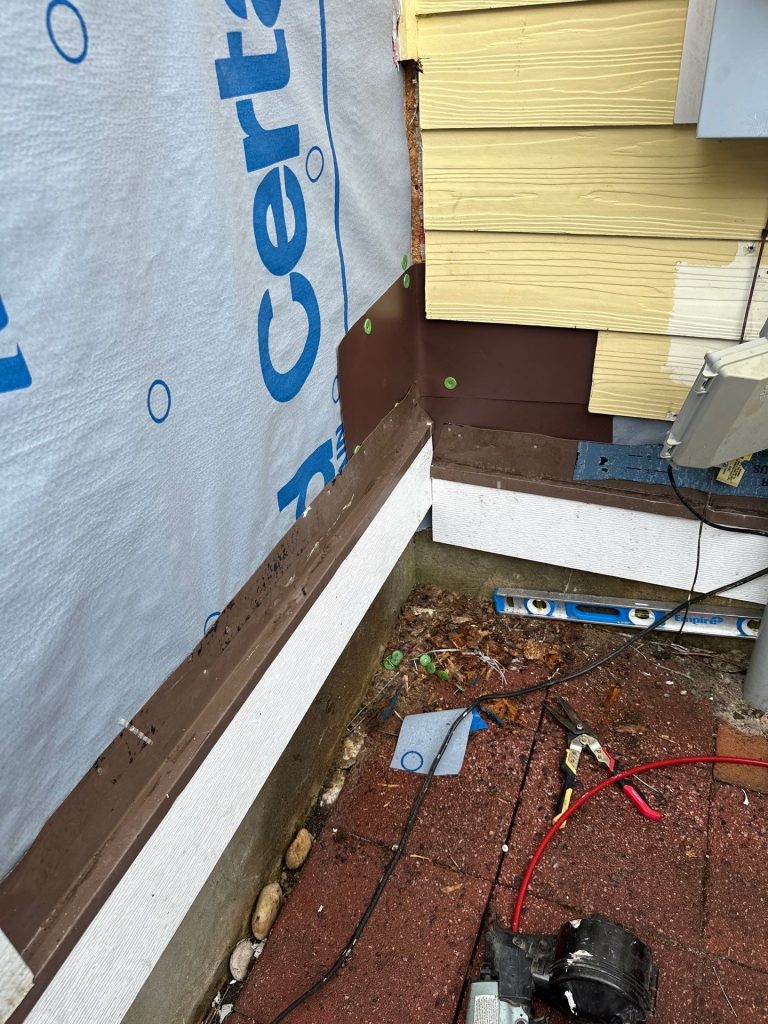 Housewrap and brown flashing around a lower exterior wall corner during rot repair in Waterford, Leland