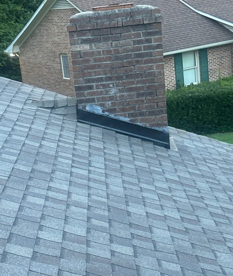 Architectural shingle courses adjoining a brick chimney and dark metal at its base