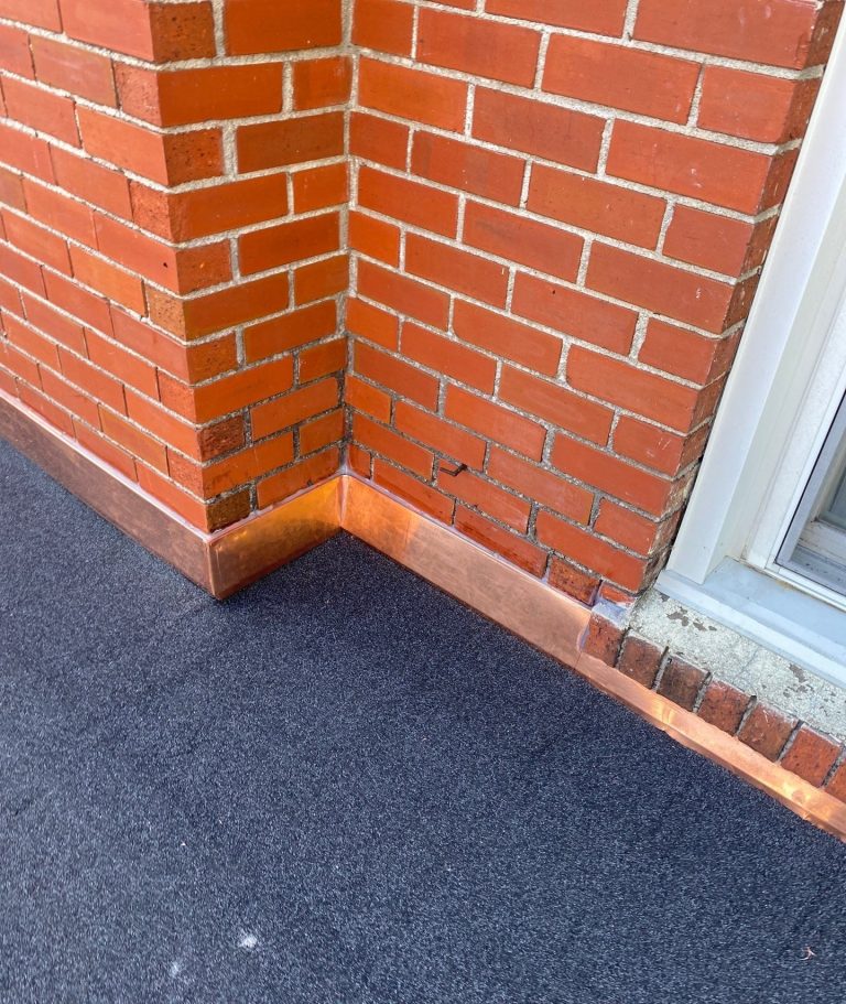 Copper flashing fitted around a projecting brick corner beside a window in Wilmington