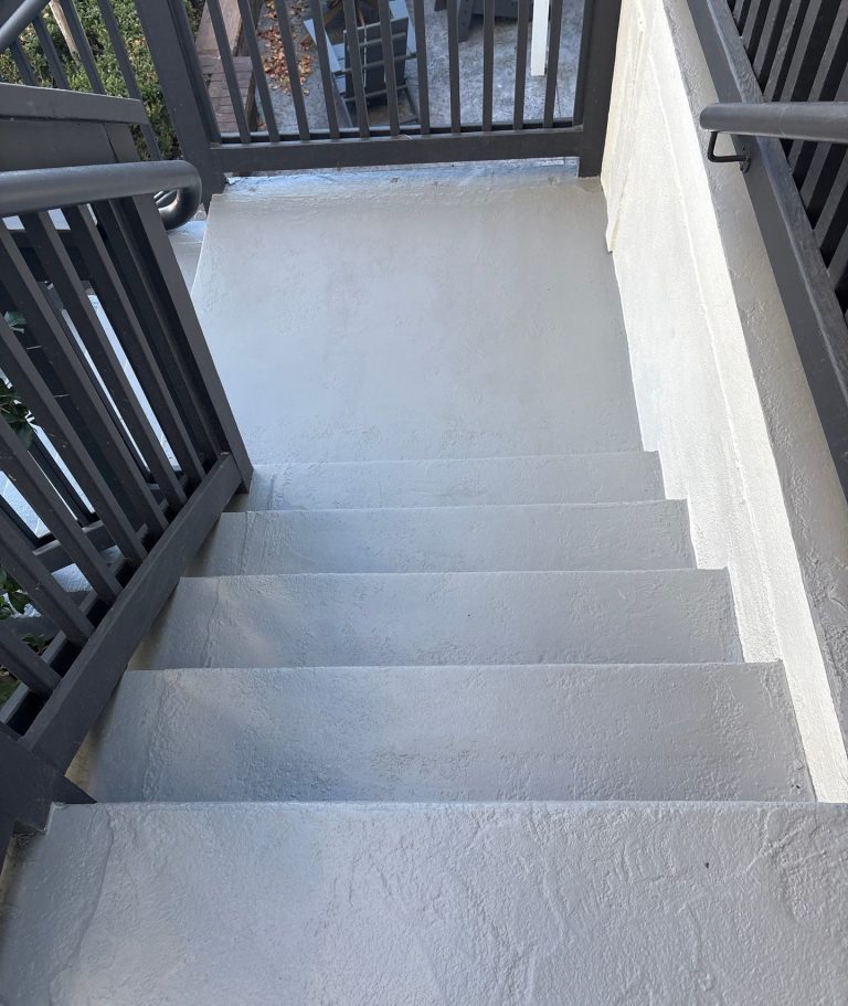 View down coated concrete steps toward a landing enclosed by dark railings